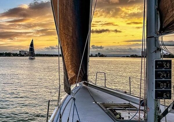 The bow of a sailing charter vessel facing a sunset over the water.
