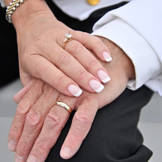Close-up of a newlywed couple’s hands displaying their wedding rings during a celebration aboard a Detroit Charter Company sailboat.