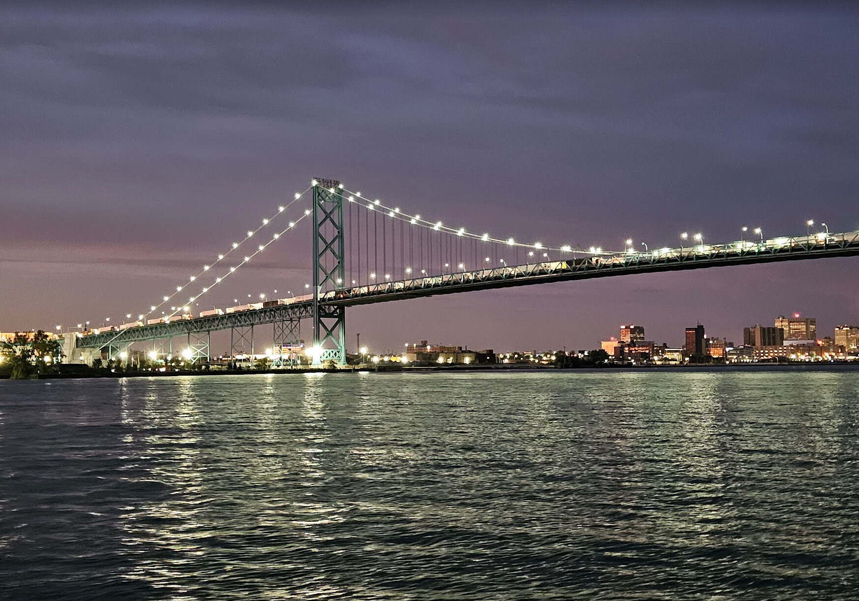A picture of the Detroit skyline and Ambassador Bridge after dark from a charter vessel