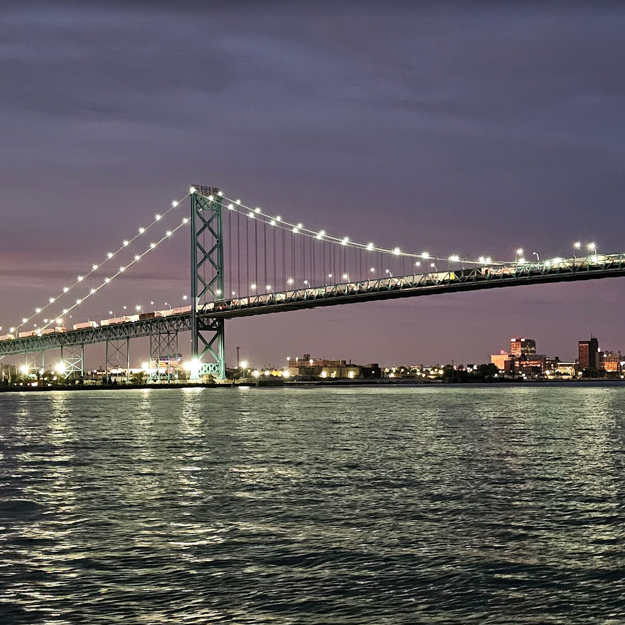 A picture of the Detroit skyline and Ambassador Bridge after dark from a charter vessel